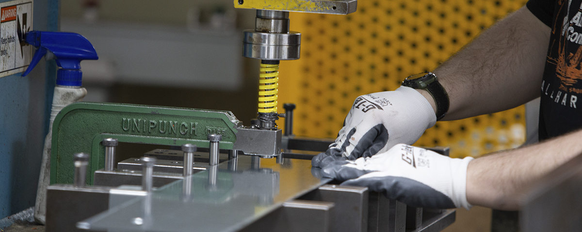 A person is operating a metal punch press, wearing gloves for safety.