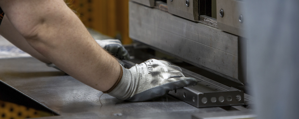 A TAC Industries employee wearing gloves is operating a machine.