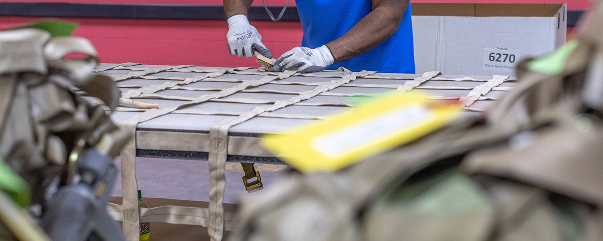 A person working with straps on a table, possibly assembling or inspecting cargo nets.