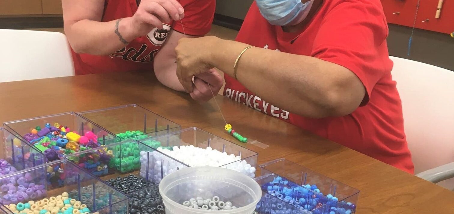 Two individuals in red shirts working together at a table, sorting colorful plastic pieces into bins.
