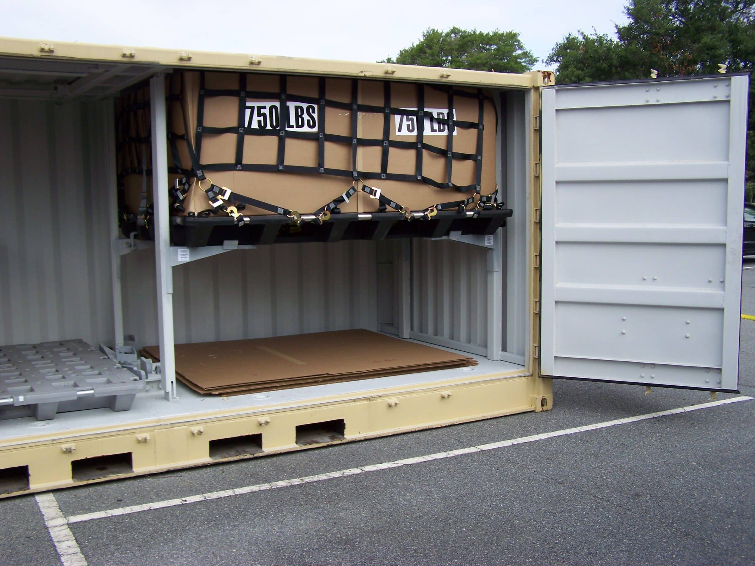 An open shipping container with secured cargo labeled "750 LBS" and a pallet and cardboard on the floor.