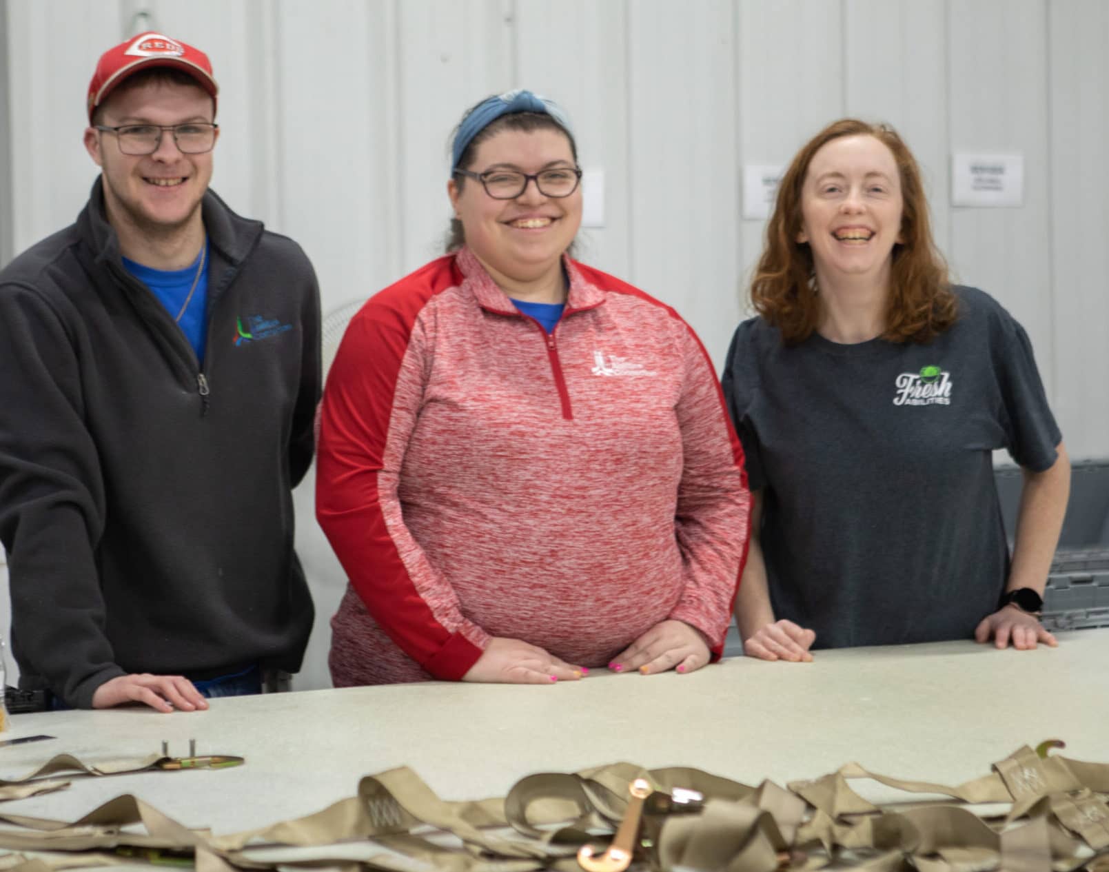 Three people smiling and standing behind a table with straps on it.