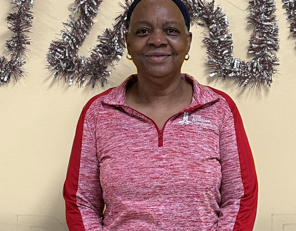 A person wearing a red pullover stands in front of a wall with tinsel decorations.
