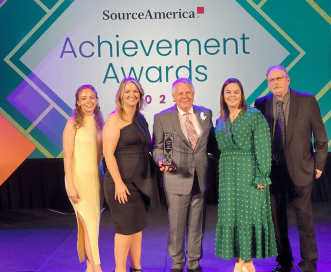 A group of five people is posed in front of signage for the SourceAmerica Achievement Awards.