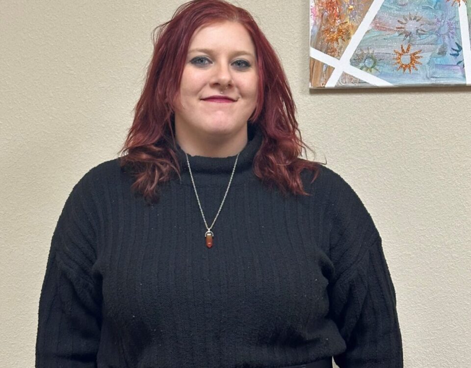 A person in a black sweater stands in front of an abstract painting, suggesting professionalism and creativity.