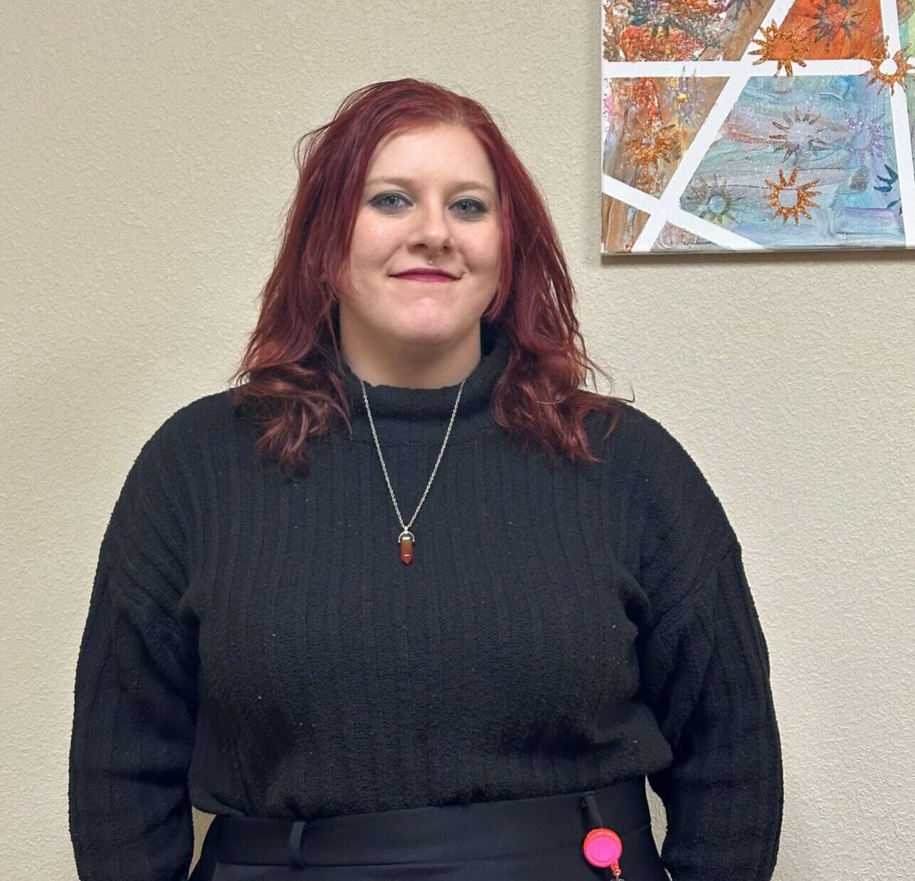 A person in a black sweater stands in front of an abstract painting, suggesting professionalism and creativity.