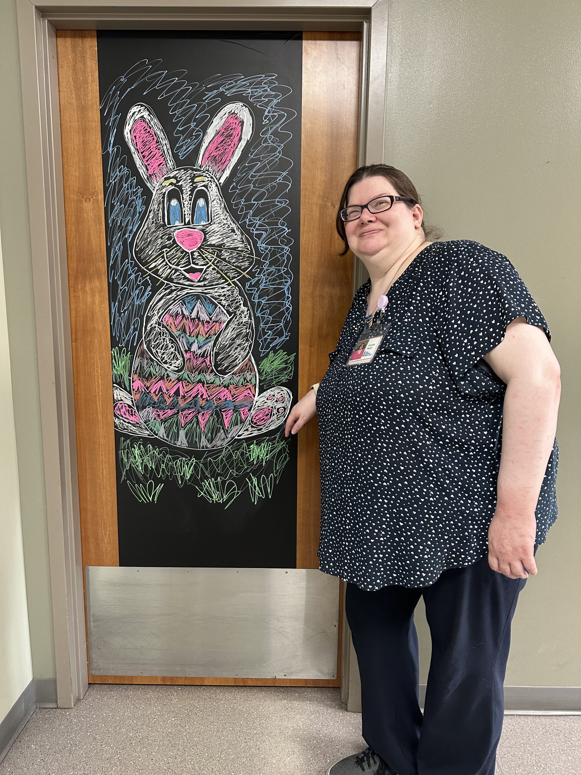 A person stands next to a colorful chalk drawing of a rabbit on a blackboard.