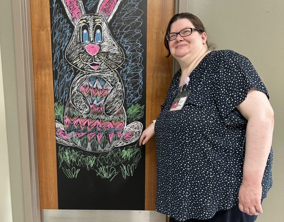 A person stands next to a colorful chalk drawing of a rabbit on a blackboard.