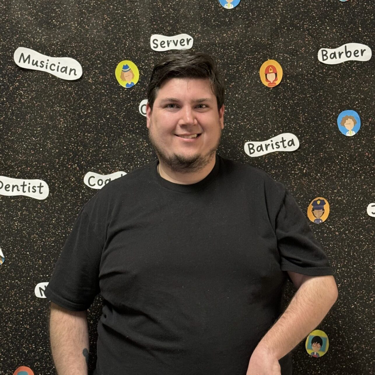 A person smiling with curly hair, wearing a necklace and a polka-dot shirt.