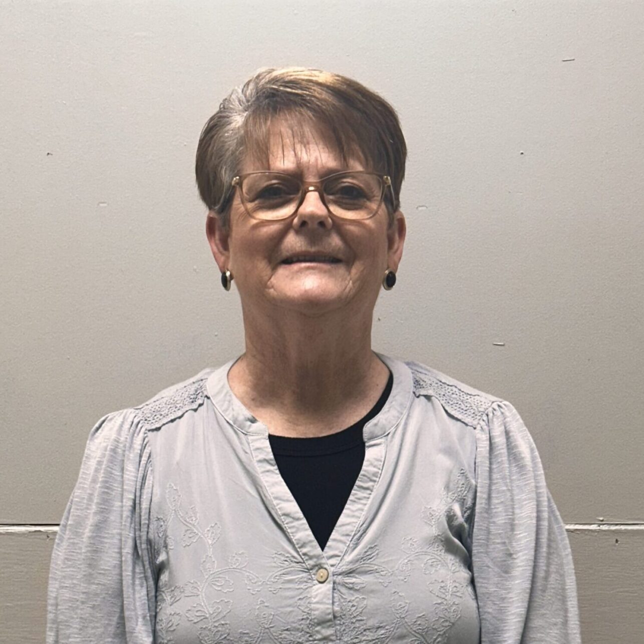A person smiling with curly hair, wearing a necklace and a polka-dot shirt.