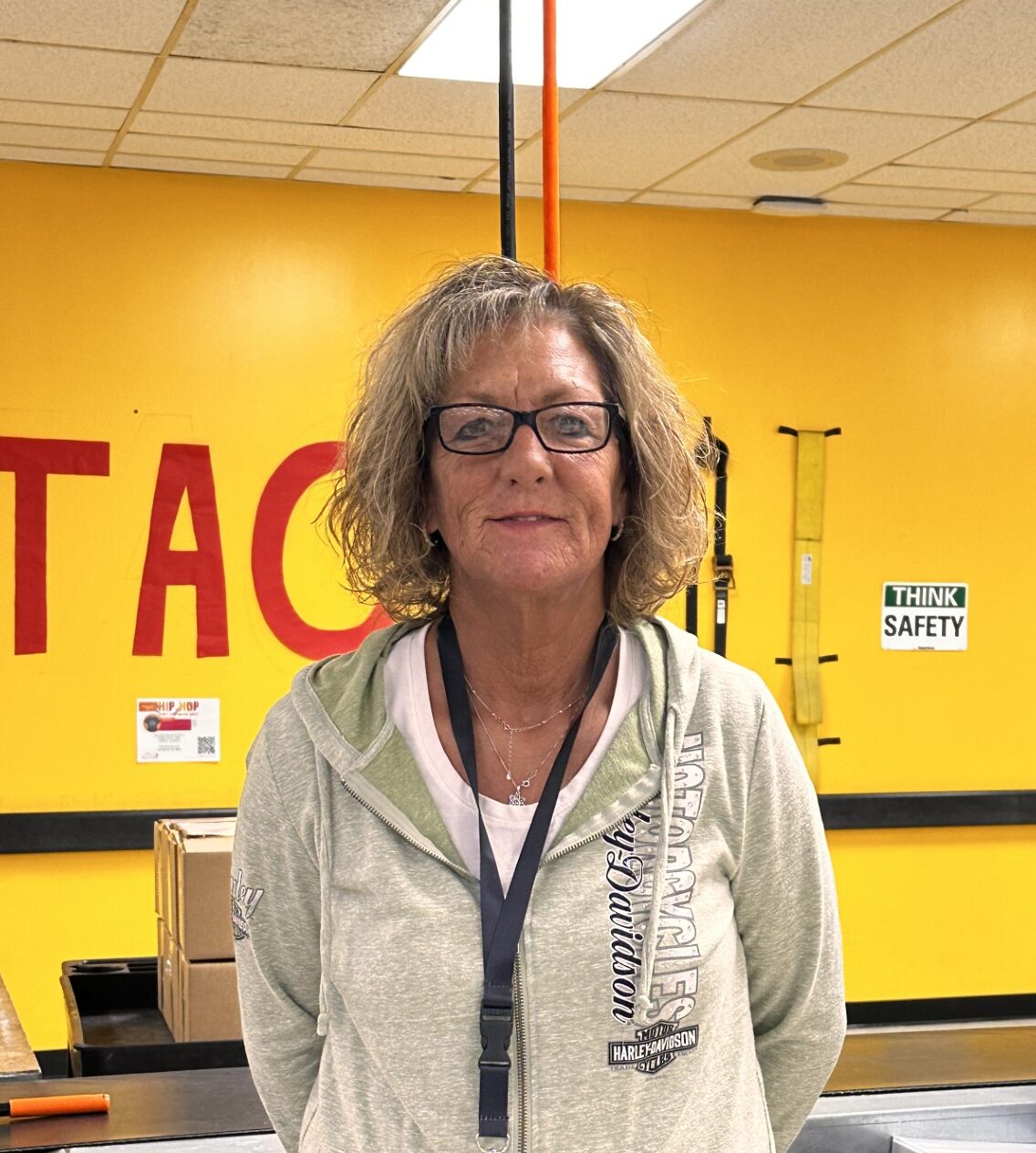 A person smiling with curly hair, wearing a necklace and a polka-dot shirt.